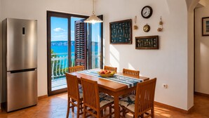 Un coin repas comprenant une table, des chaises, un réfrigérateur et une vue sur la mer, visible à travers une porte vitrée.