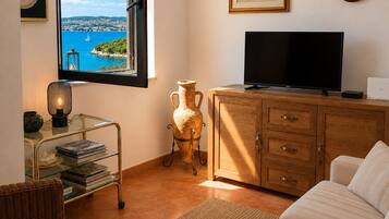Una sala de estar con una televisión, un jarrón, una estantería y vistas a una masa de agua a través de una ventana.