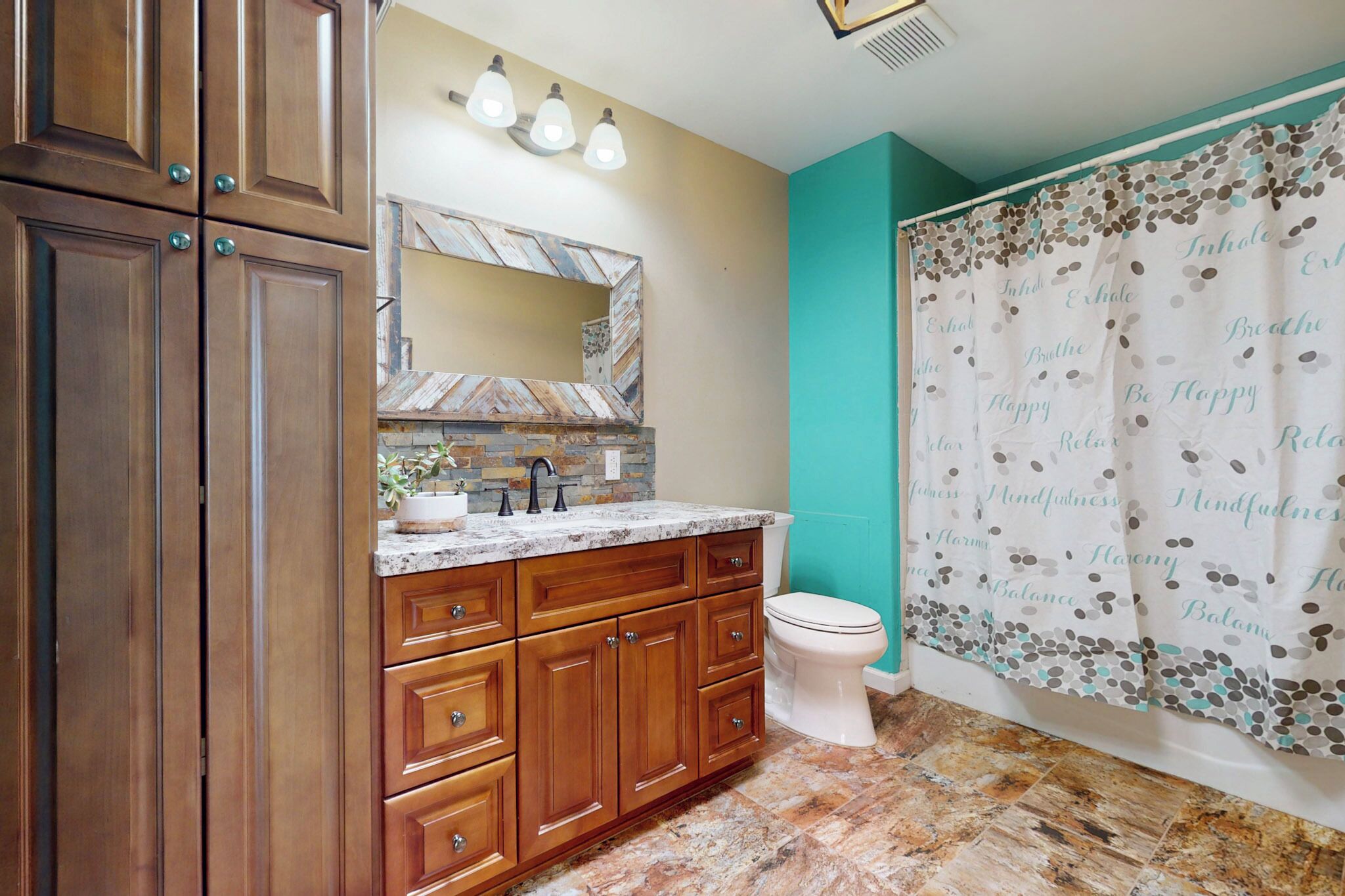 A bathroom with wooden cabinets, a marble countertop, a white toilet, and a teal shower curtain with motivational text.