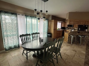 A dining area with a round table and chairs, a kitchen with wooden cabinets, and a stone-tiled floor.