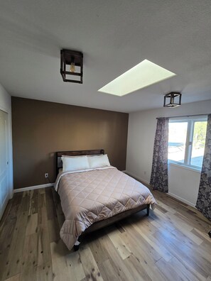 Un dormitorio con cama, tragaluz, ventana con cortinas y suelo de madera.
