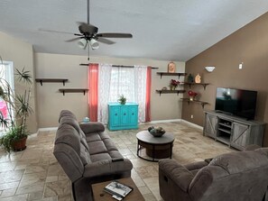 A living room with a sofa, a coffee table, a TV, a ceiling fan, and a window with curtains. - Entire Desert Hacienda Estate Compound - Sleeps 12 in La Mesilla, New Mexico (Española)