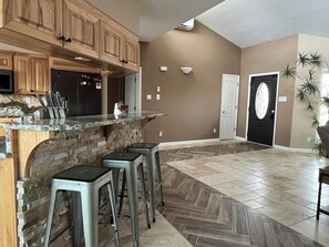 Cocina con armarios de madera, encimera de granito y estufa integrada. Hay tres taburetes de bar y una puerta con panel de vidrio decorativo.