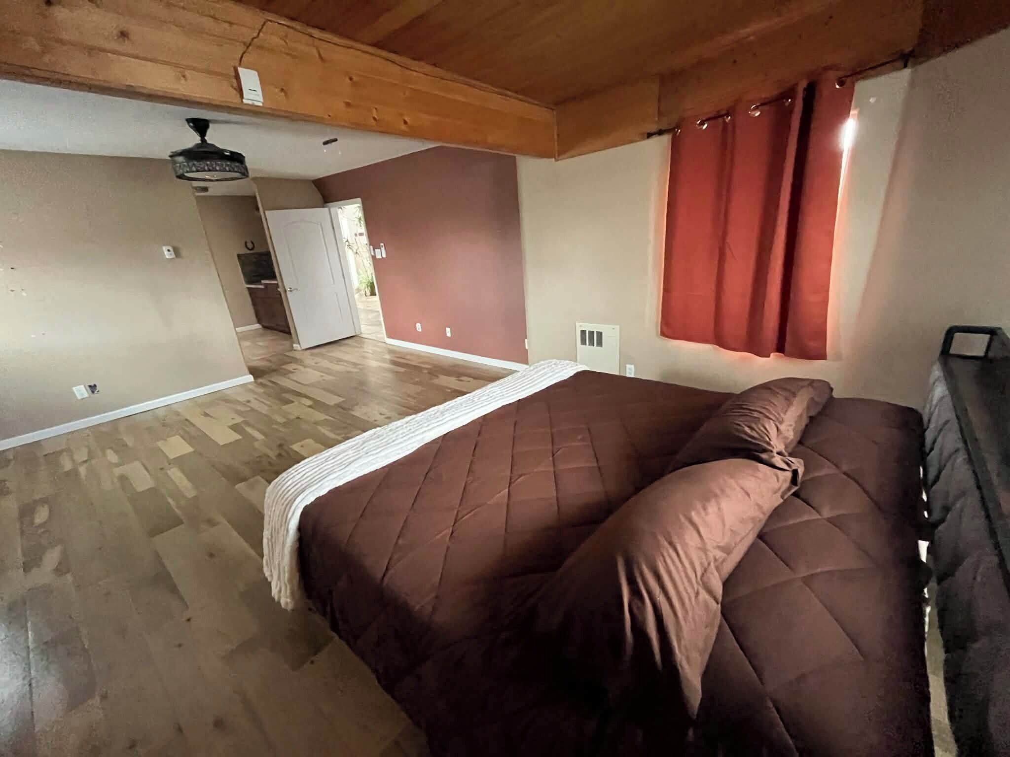 Ein Schlafzimmer mit einem großen Bett, Holzbalkendecke, einer Tür zu einem anderen Raum und einem Fenster mit Vorhängen.