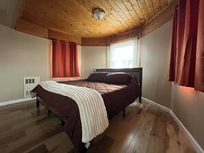 Ein Schlafzimmer mit Holzbalkendecke, einem Bett mit weißer Decke und roten Vorhängen.
