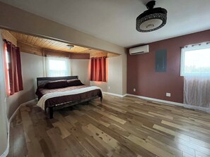 A bedroom with a bed, wooden flooring, a ceiling fan, and an air conditioning unit. - Entire Desert Hacienda Estate Compound - Sleeps 12 in La Mesilla, New Mexico (Española)