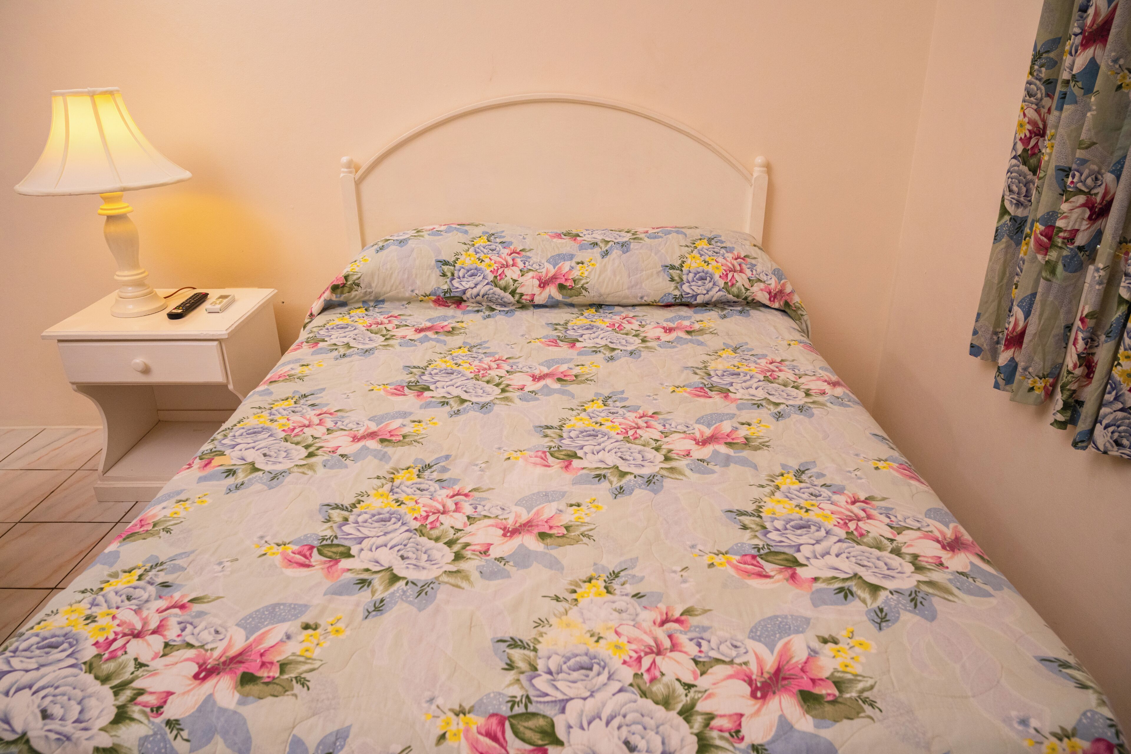 A bed with a floral bedspread, a bedside table with a lamp, and a curtain.