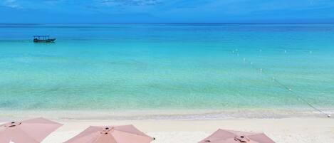 A beach with clear turquoise water, a boat in the distance, and umbrellas on the sand.