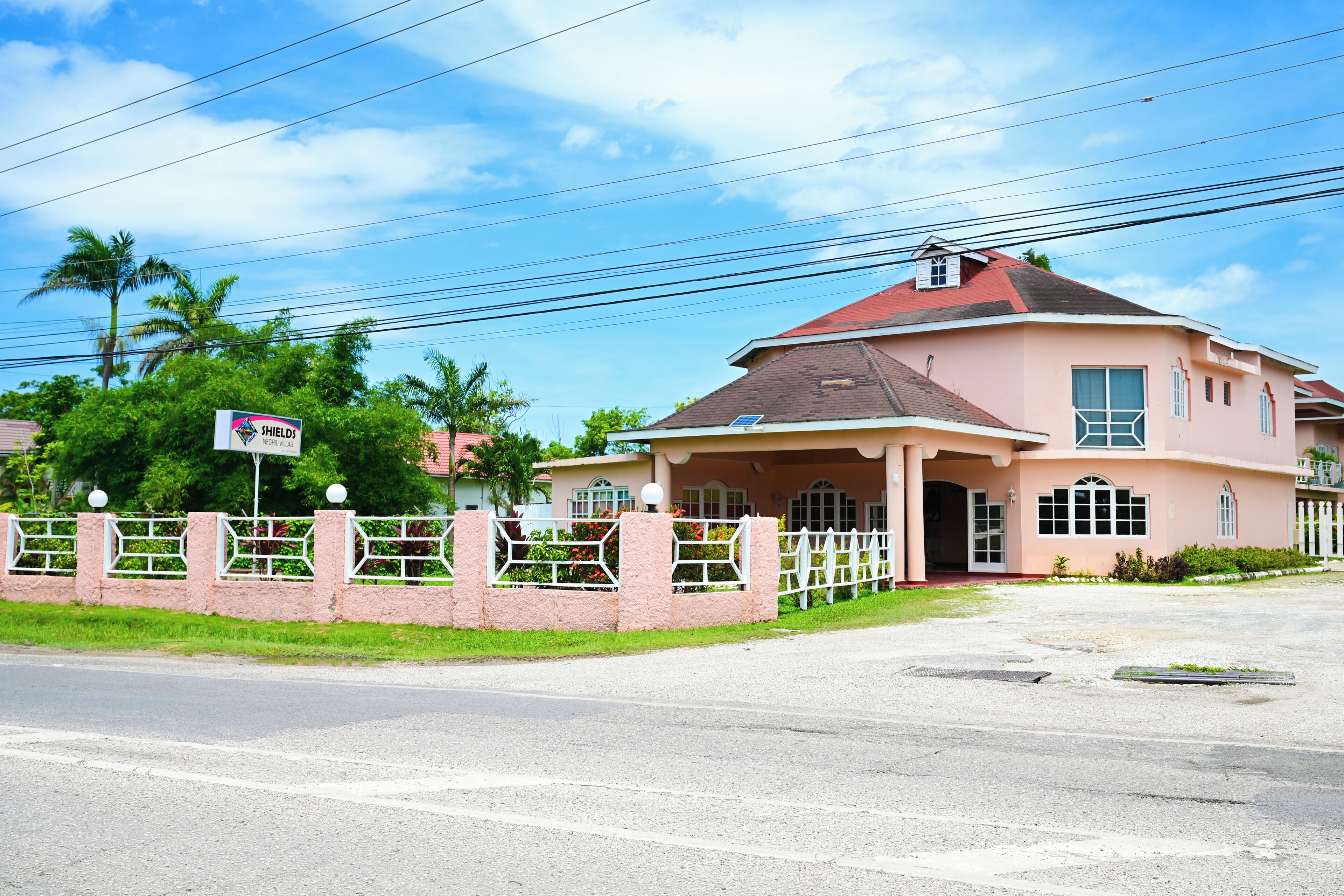 A two-story house with a red roof, a gated entrance, and a signboard.