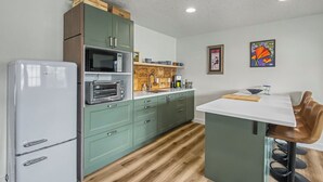A kitchen with a refrigerator, microwave, and oven, wooden cabinets, a wooden countertop, and a dining area with a chair and table. - Cute clean cottage with modern amenities near downtown (McMinnville)