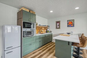 A kitchen with a refrigerator, microwave, and oven, wooden cabinets, a wooden countertop, and a dining area with a chair and table. - Cute clean cottage with modern amenities near downtown (McMinnville)