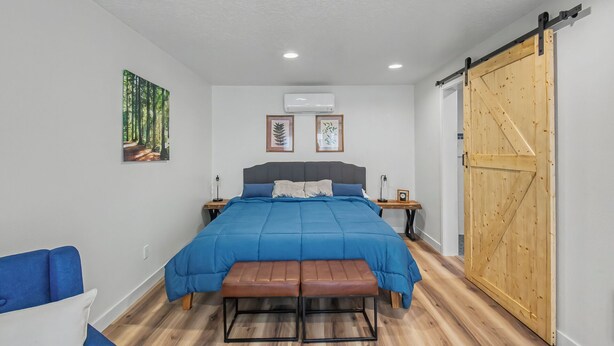 A bedroom with a bed, a bench, a wooden door, and two wall-mounted air conditioners. - Cute clean cottage with modern amenities near downtown (McMinnville)