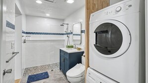 A modern bathroom with a built-in washing machine, a shower, and a toilet. - Cute clean cottage with modern amenities near downtown (McMinnville)