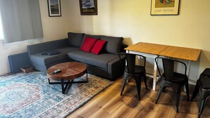 A living room with a grey sofa, a small round table, a wooden dining table with two chairs, a patterned rug, and two framed pictures on the wall. - Cute clean cottage with modern amenities near downtown (McMinnville)