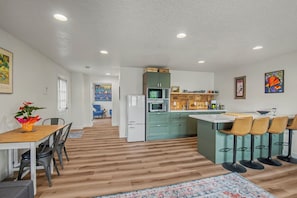A modern kitchen with a central island, bar stools, and a dining area with a table and chairs. - Cute clean cottage with modern amenities near downtown (McMinnville)