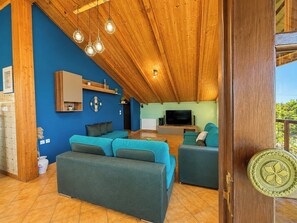 A modern living space with a wooden ceiling, blue walls, and a large TV. - Evoikos Blue Villa-Sea View & Garden for 5 by ΜΡS (Agii Apostoli)