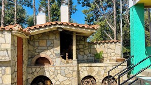 Une cuisine extérieure en pierre, dotée d’une cheminée, d’un foyer et d’un escalier menant à un niveau supérieur.