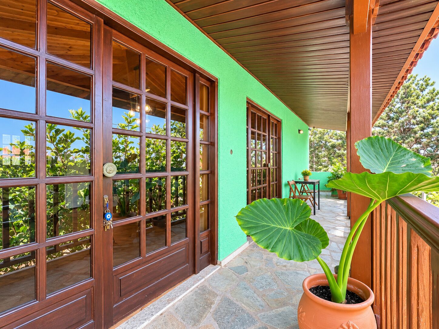 A covered porch with large windows and a potted plant.