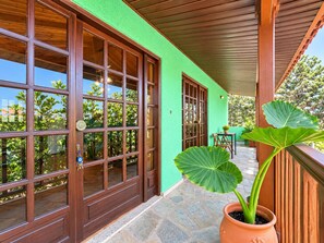 A covered porch with large windows and a potted plant.