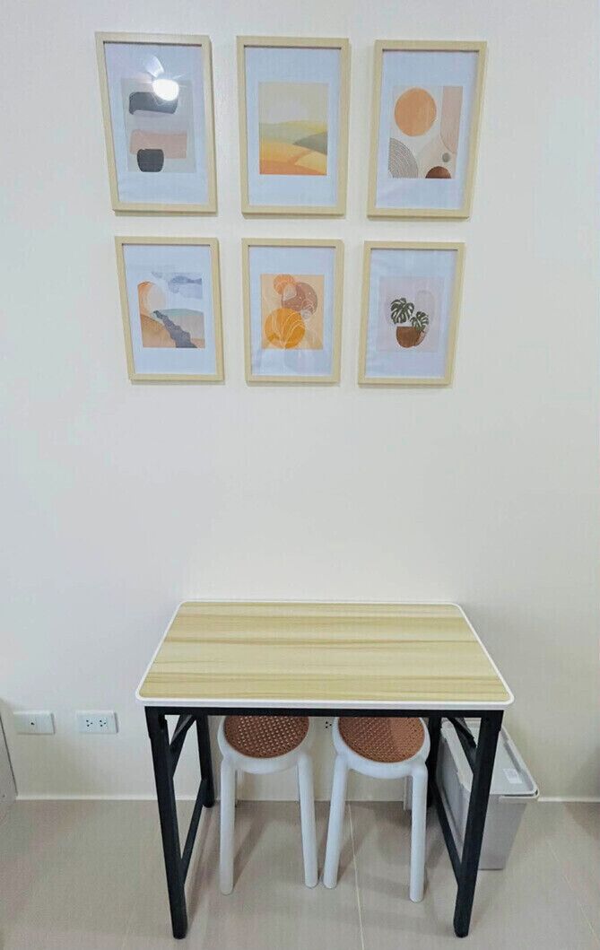 A small dining area with a table and two chairs, a wall with six framed artworks, and a white wall with a power outlet.