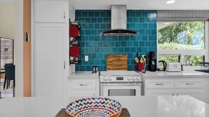 A modern kitchen with white cabinetry, a teal backsplash, and a stainless steel range hood. - Nacho's Place! (Palm Springs)
