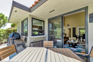 Una terrazza esterna con tavolo e sedie, un barbecue e un'ampia vetrata scorrevole che dà su un ambiente interno.