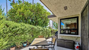 An outdoor patio with a dining table and chairs, surrounded by greenery and a view of the house interior. - Nacho's Place! (Palm Springs)