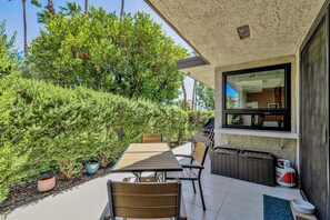 Eine Außenpatio mit Esstisch und Stühlen, umgeben von viel Grün und Blick ins Hausinnere.