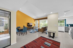 A modern living room with a dining area, a kitchen, and a large window providing natural light. - Nacho's Place! (Palm Springs)