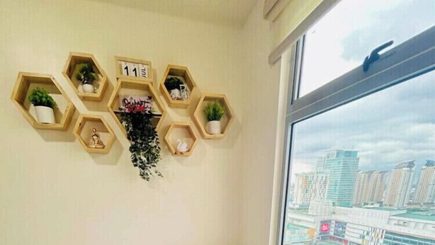 Ein Hotelzimmer mit einem Bett, einem Fenster mit Blick auf die Stadt und einem an der Wand befestigten Regal mit Pflanzen und einer Uhr.