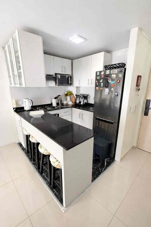 A modern kitchen with a central island, white cabinets, a stainless steel refrigerator, and a microwave above the island. - Family 2BR 2 Baths, Walk to La Moneda-Free Parking (Santiago)