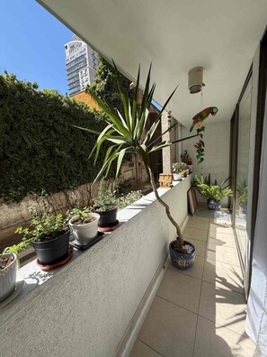 A balcony with potted plants, a hanging birdcage, and a view of a building in the background. - Family 2BR 2 Baths, Walk to La Moneda-Free Parking (Santiago)