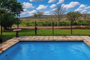Una piscina con vistas a un jardín cercado y colinas al lejano.