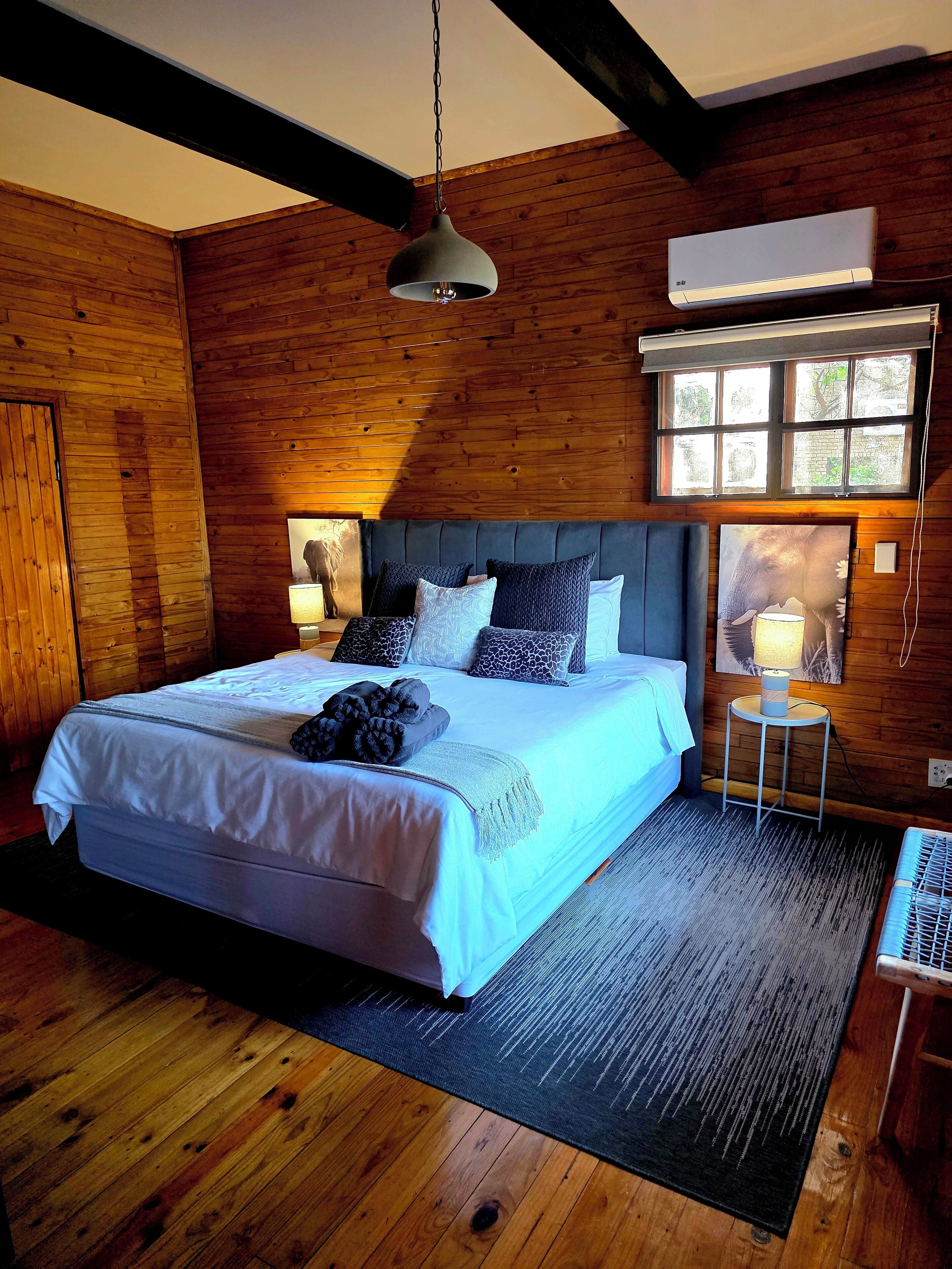 A bedroom with a bed, bedside lamps, a window, and a wall-mounted air conditioner.