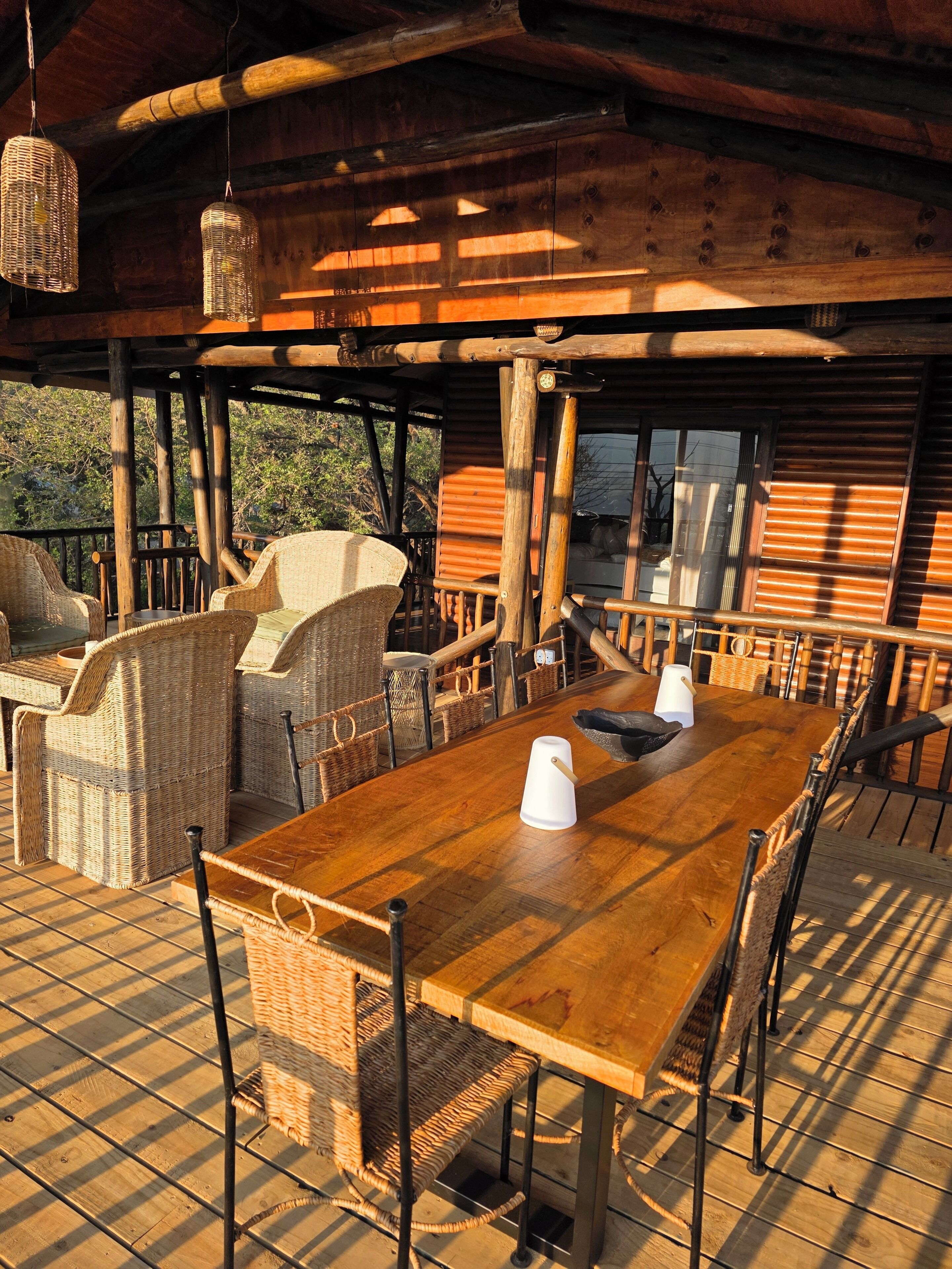 Una terraza al aire libre de madera con muebles de mimbre, una mesa de madera y lámparas colgantes de mimbre.