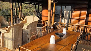 Una terraza al aire libre de madera con muebles de mimbre, una mesa de madera y lámparas colgantes de mimbre.