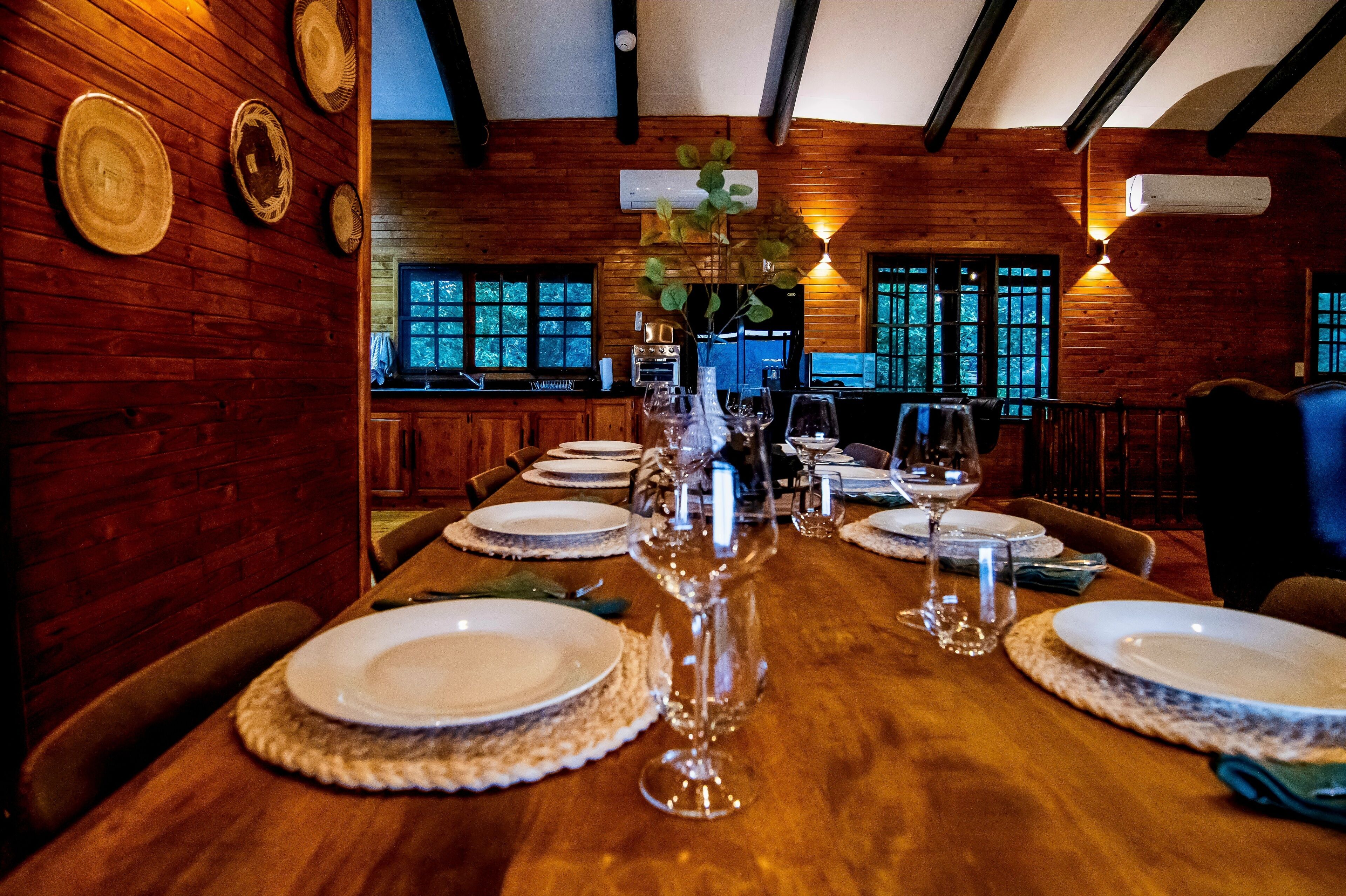 A wooden dining table set for a meal with plates, glasses, and a vase.
