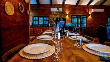 A wooden dining table set for a meal with plates, glasses, and a vase.