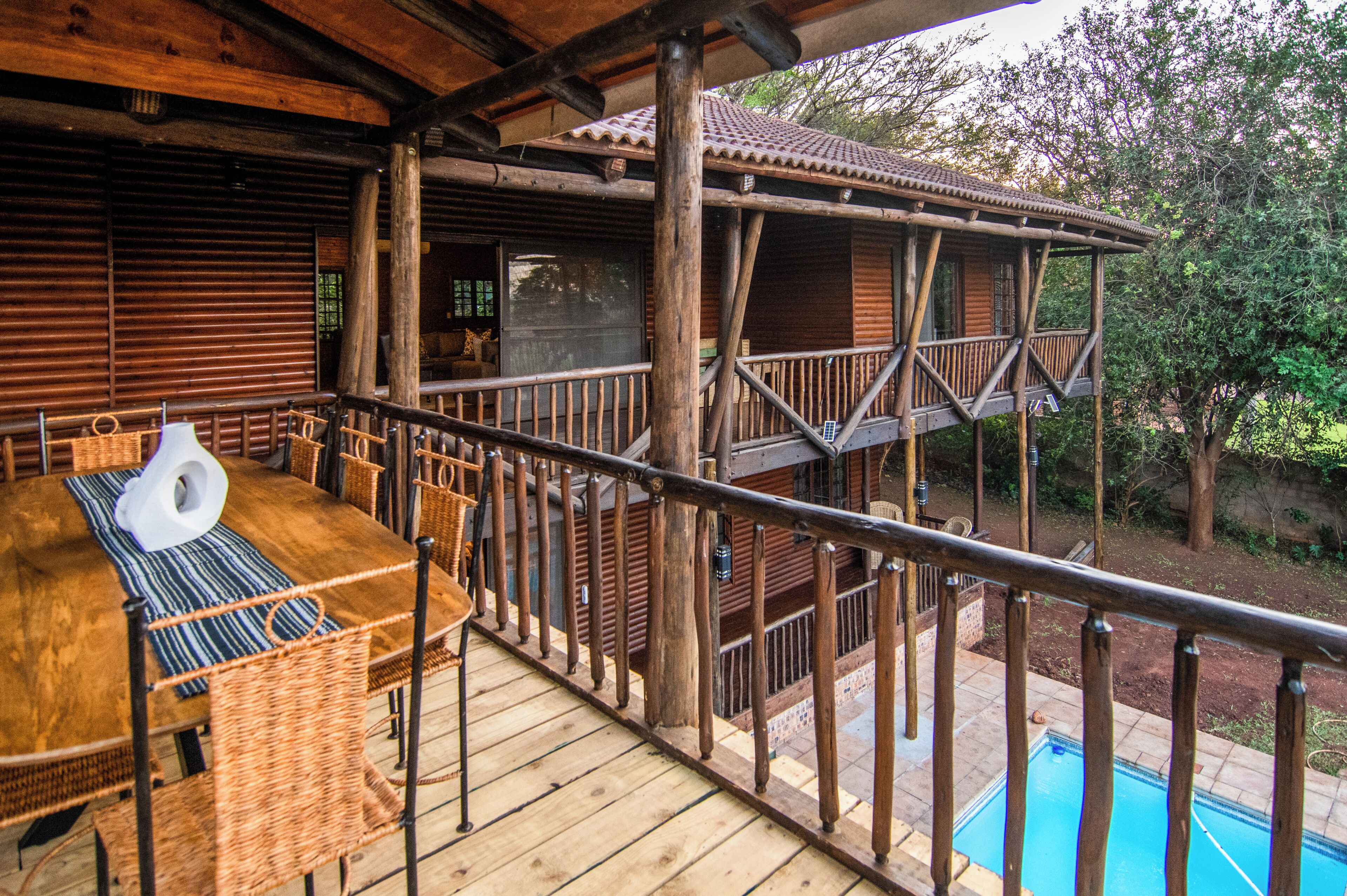 A wooden deck with a pool, outdoor seating, and a covered area with a view of trees.