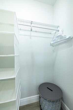 A storage closet with shelves, a hanging rack, and a round trash bin. - Cozy Family Haven with Arcade (Tampa)