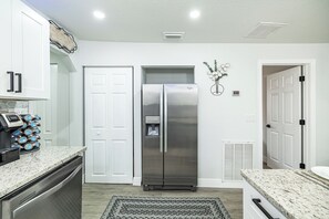 A kitchen with white cabinets, a stainless steel refrigerator, a coffee machine, and a patterned rug. - Cozy Family Haven with Arcade (Tampa)