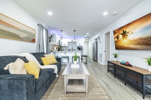 Ein modernes Wohnzimmer mit einem grauen Sofa, einem Couchtisch und einer Küche im Hintergrund.