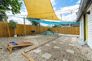 Ein Garten mit Holzzaun, Grill, Gartenmöbeln und einer schattigen Sitzgelegenheit mit Lichterketten.