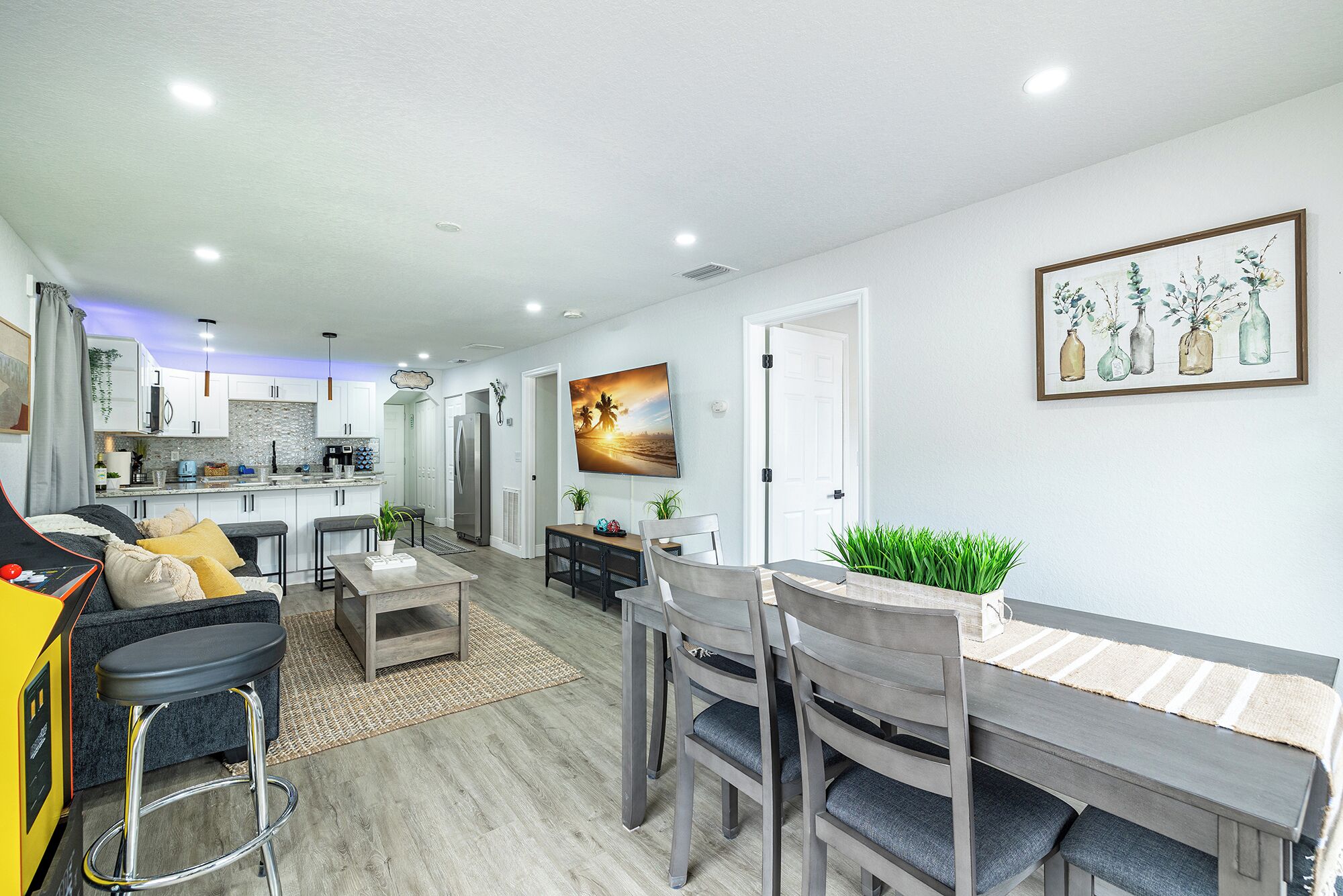 A modern living room with a dining area, kitchen, and a large painting on the wall.