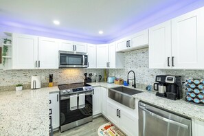 A modern kitchen with white cabinets, stainless steel appliances, and a herringbone tile backsplash. - Cozy Family Haven with Arcade (Tampa)