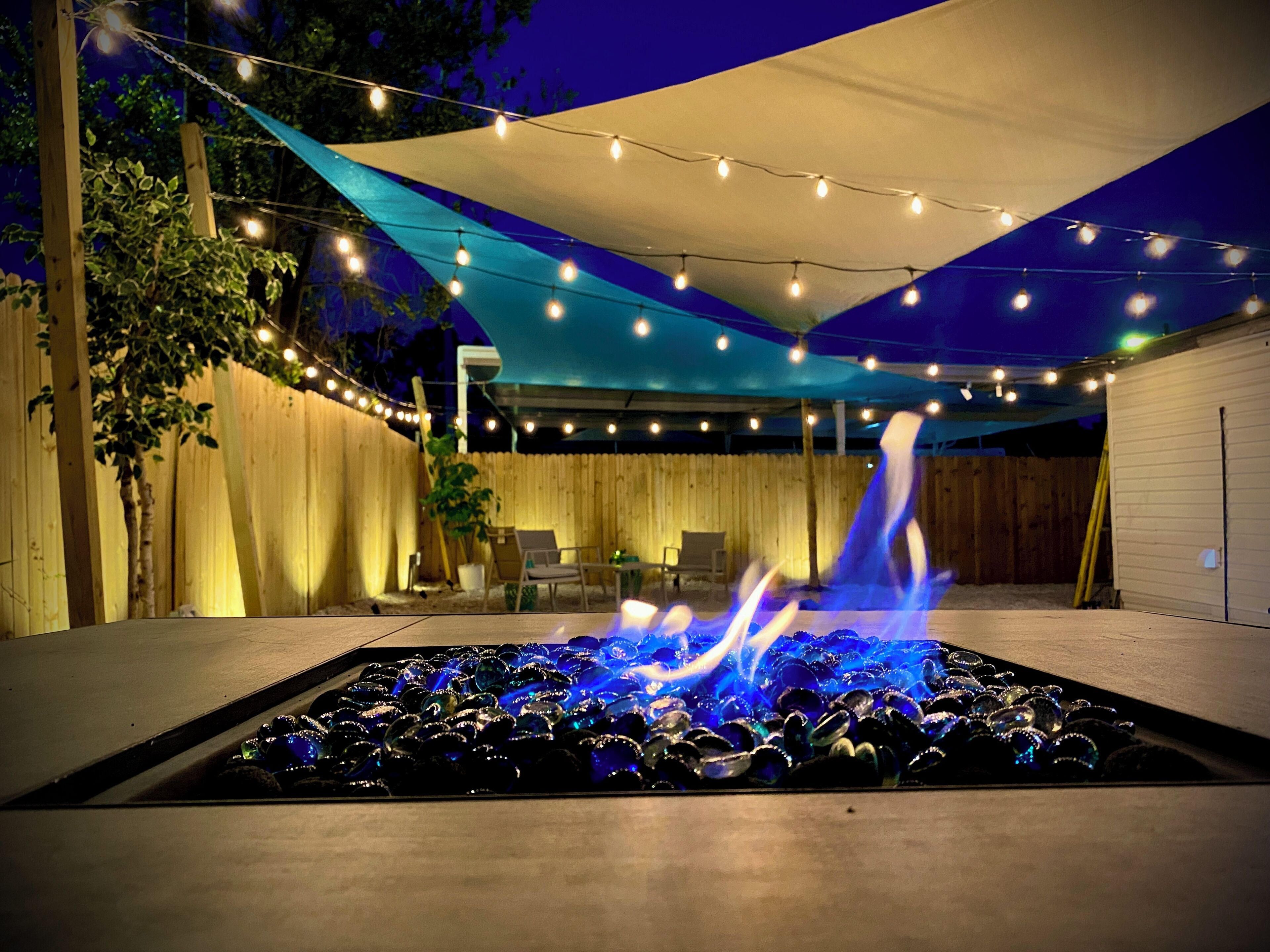 Un patio exterior con una chimenea, luces colgantes y una zona de estar cubierta.