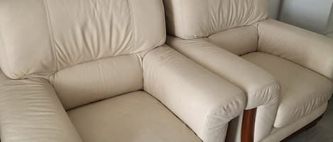 A beige leather sofa with wooden legs, positioned against a white wall with a clock.