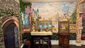 Ein Zimmer mit einer Steinwand, einem Kamin, einem Wandteppich und einem kleinen Tisch mit Spiegel und Blumen.