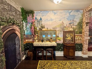 Ein Zimmer mit einer Steinwand, einem Kamin, einem Wandteppich und einem kleinen Tisch mit Spiegel und Blumen.