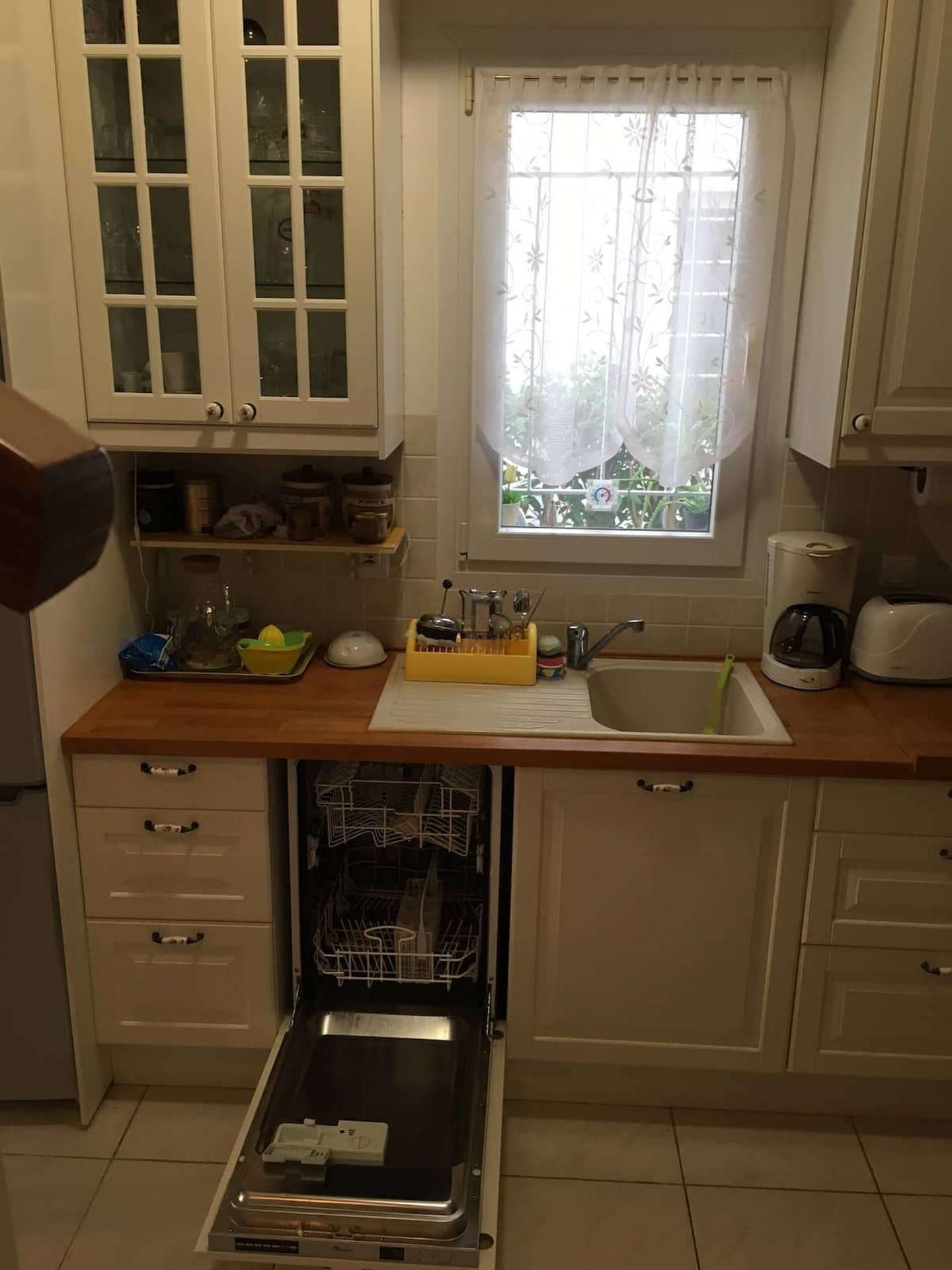 A compact kitchen with white cabinets, a window with floral curtains, a sink, and a dishwasher.